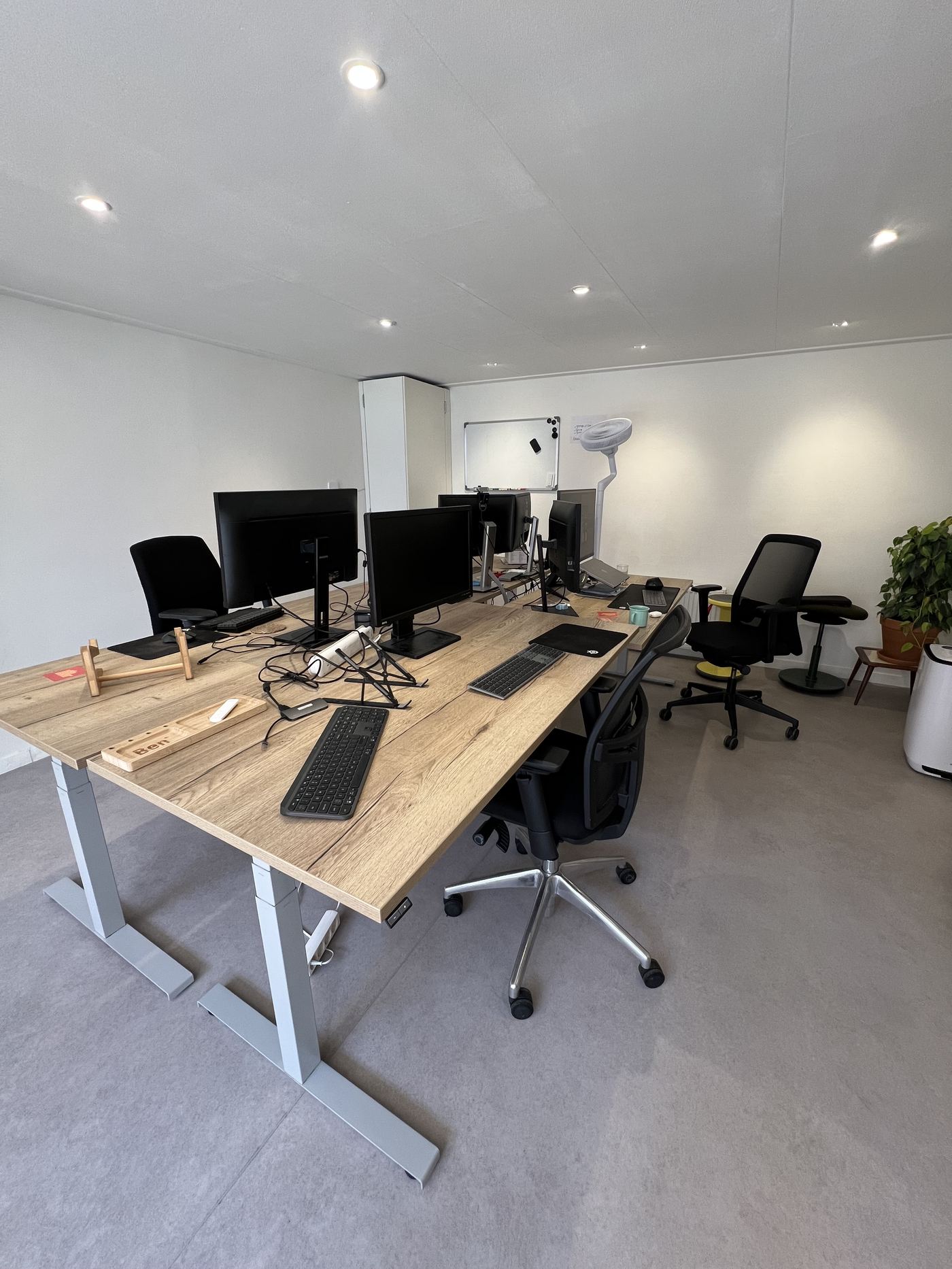 De werkruimte met houten zit-sta bureaus, beeldschermen en bureaustoelen.
